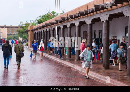 Persone che camminano su asfaltatrici bagnate di mattoni rossi di fronte al Palazzo dei governatori dopo una tempesta di pioggia monsonica, Santa Fe, New Mexico, Stati Uniti Foto Stock