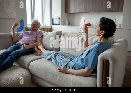 Coppia anziana stressata che soffre di calore, che si apre sul divano non funziona. Gli anziani lottano Foto Stock