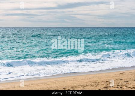 Le onde turchesi dell'oceano si lavano delicatamente su una spiaggia di sabbia dorata in un giorno nuvoloso Foto Stock