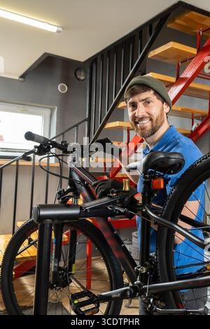 Meccanico di biciclette che indossa un berretto verde e una polo blu che ispeziona la bicicletta Foto Stock