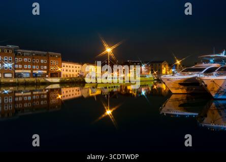 Le luminose luci di strada gettano le forme delle stelle e i riflessi nelle acque fisse di Poole Quay Foto Stock