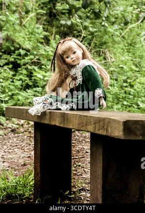 Una bambola in un abito verde si trova su una panchina di legno in un ambiente boschivo. Foto Stock