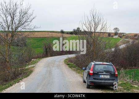 un'auto nera parcheggiata sul lato della strada curva in campagna e nei campi e nelle fattorie Foto Stock