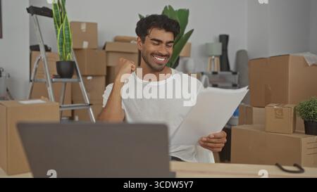 L'uomo tiene in mano documenti in movimento e pompe per la prima volta in un edificio pieno di scatole di cartone impilate; gioia di successo. Foto Stock