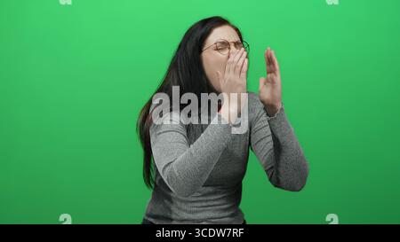 Donna con occhiali mostra espressioni su uno sfondo verde brillante indossando un maglione grigio che cattura l'emozione e la bellezza naturale Foto Stock