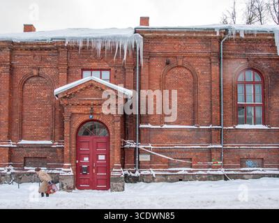 19 dicembre 2010, Tartu, Estonia: Vista frontale di un edificio in mattoni rossi a Tartu con lunghi ghiacci appesi al tetto e un pedone in tessuto invernale Foto Stock