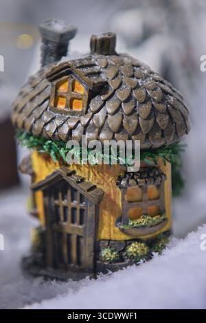 Cottage in miniatura con finestre lucenti in uno studio innevato, arredamento stravagante per le vacanze girato all'interno per licenze commerciali e editoriali. Foto Stock