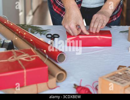 Mani di donna che usano il nastro per avvolgere i regali di Natale in carta rossa Foto Stock