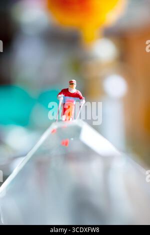 Una figura sciatrice in miniatura a metà salto sembra volare attraverso uno sfondo colorato e astratto, creando una scena surreale e dinamica. Foto Stock