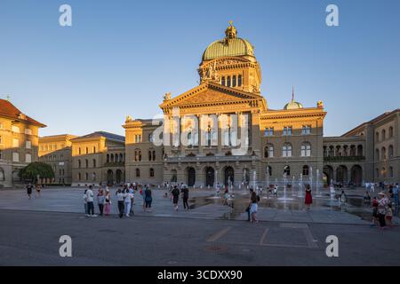 07-08-2025 Berna, Svizzera. Persone di fronte all'edificio del Parlamento. Luce del tramonto estiva, giochi per bambini alle fontane, vista grandangolare Foto Stock