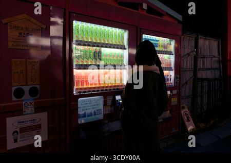 Donne che scelgono un drink in un distributore automatico illuminato di notte ad Asakusa Foto Stock