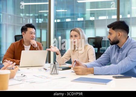 Un incontro di lavoro collaborativo tra diversi colleghi che discutono idee e strategie in un ambiente di ufficio moderno. Il gruppo è concentrato e coinvolgente con documenti e un notebook Foto Stock