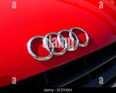 Derby, Regno Unito - 14 agosto 2025: Primo piano dell'iconico logo Audi a quattro anelli esposto all'esterno di un'auto rossa, che mette in risalto i marchi eleganti A. Foto Stock