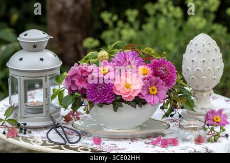 composizione floreale di rosa, dahlia, ortensie in fiore e anemoni giapponesi in una barca per salsa e una lanterna nel giardino Foto Stock