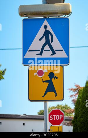Un cartello blu di attraversamento pedonale sopra un cartello di avvertimento giallo che raffigura un bambino con in mano un lecca lecca. Indica un'area di attraversamento vicino a una scuola o a un playgroun Foto Stock
