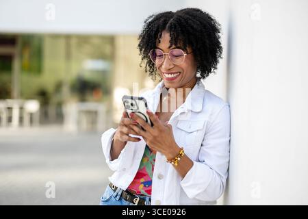 Ritratto di una giovane donna sorridente che usa il telefono cellulare in città Foto Stock
