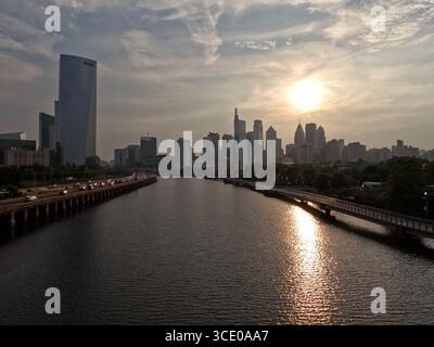 Il sole sorge dietro lo skyline di Philadelphia, visto dal ponte di South Street. Foto Stock
