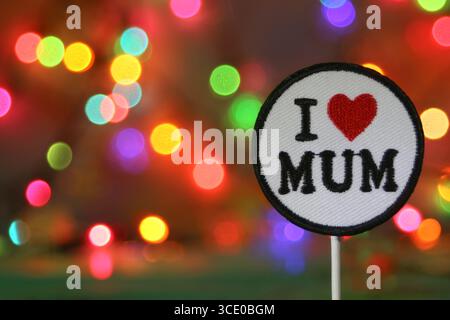 Patch ricamata "i Love Mum" con cuore rosso su sfondo bokeh arcobaleno, lasciando spazio per il testo. Festa della mamma o concetto di vacanza. Foto Stock