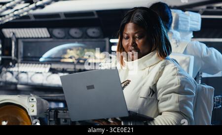 L'astronauta di ritorno dalla superficie del pianeta togliendo il casco, parlando con un collega che usa il laptop per verificare i parametri. Cosmonauta che termina la spedizione chiacchierando con il collega che aggiorna il registro di volo Foto Stock