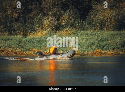 un pescatore su una barca galleggia lungo il fiume con canne da pesca Foto Stock