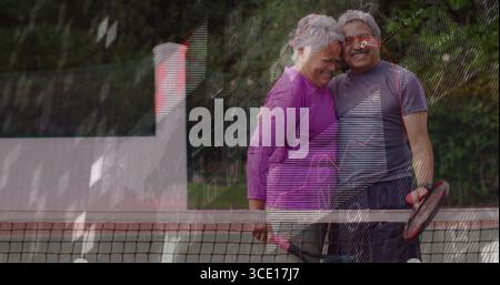 Coppia senior sorridente appoggiata su una rete da tennis all'aperto con linee di confine e racchette Foto Stock