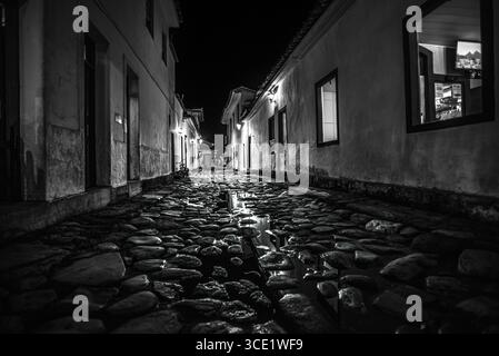 Vista notturna in bianco e nero dell'architettura coloniale e delle pietre umide a Paraty, Brasile Foto Stock