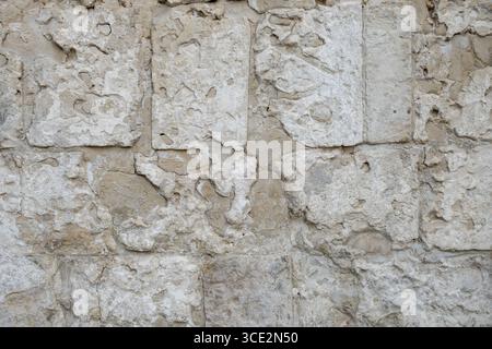 Primo piano di una parete in pietra testurizzata che mostra usura ed erosione naturali. La superficie in pietra presenta motivi irregolari e robusti e varie tonalità, per catturare immagini Foto Stock