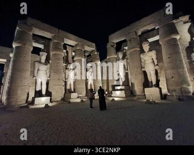 La sala peristilia del tempio di Luxor, costruita da Ramses II, illuminata di notte, fiancheggiata da colonne di loto e statue colossali del faraone. Foto Stock