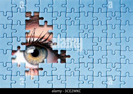 Primo piano dell'occhio umano che guarda attraverso i pezzi mancanti del puzzle, il concetto di curiosità e mistero Foto Stock