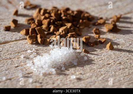 Primo piano di cristalli di zucchero grossolani e granuli di caffè solubile sparsi su una superficie in legno ruvida. Contrasto elevato e illuminazione naturale esaltano il Foto Stock