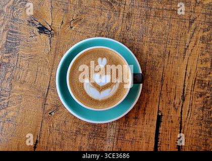 Tazza di caffè color azzurro su un piattino. Tazza di caffè a forma di cuore collocato su un vecchio tavolo di legno. Foto Stock
