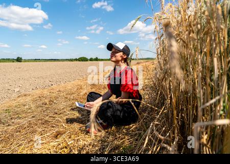 Lavoratrice agricola moderna che si prende una pausa con un tablet sul campo Foto Stock