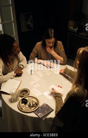 Giovani donne multietniche che leggono e interpretano le carte dei Tarocchi intorno al tavolo Foto Stock