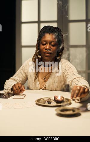 Giovane donna nera adulta che esegue la lettura della carta dei Tarocchi con incenso bruciante Foto Stock