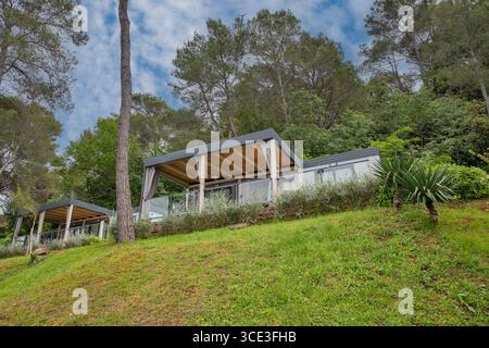 Moderne case mobili con terrazze coperte posizionate su verdi colline terrazzate tra alberi di pino e vegetazione mediterranea nel resort croato. Foto Stock
