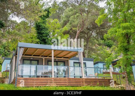 Moderne case mobili con terrazze coperte posizionate su verdi colline terrazzate tra alberi di pino e vegetazione mediterranea nel resort croato. Foto Stock