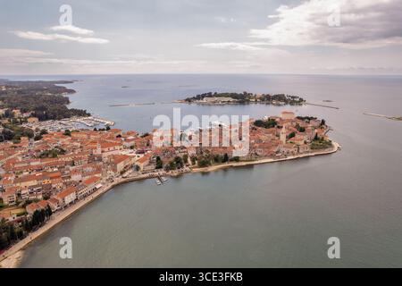 Vista aerea dall'alto dell'affascinante città costiera di Porec, Croazia, con tetti in terracotta, un vivace porto turistico e il vasto mare Adriatico sotto un tetto parzialmente coperto Foto Stock