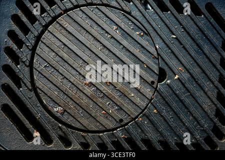 Una griglia nera con un foro al centro. La grata è sporca e contiene alcune particelle di cibo. Foto Stock