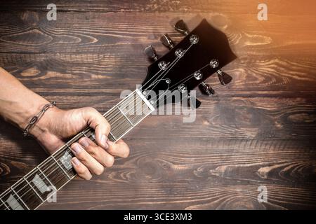 Musica, suono. Mano del musicista che tiene il collo di una chitarra elettrica basso isolato su uno sfondo vintage in legno. Foto Stock