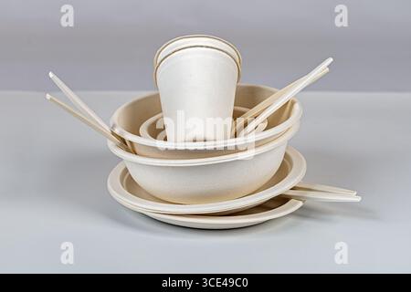 Piatti, ciotole e tazze biodegradabili impilati con bacchette su sfondo neutro, che presentano stoviglie monouso ecologiche Foto Stock