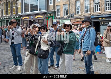 Edimburgo, Sotland, Regno Unito. 15 agosto 2025. Festival Fringe Day 15 è caldo ma coperto, la temperatura è di 22 gradi centigradi per i visitatori e gli artisti di strada. Nella foto: I turisti asiatici fotografano un ciclista. Credito: Arch White/alamy notizie dal vivo. Foto Stock
