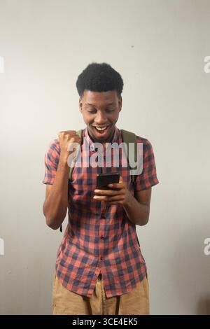 teenager nero che trasporta lo zaino utilizzando lo smartphone che esprimono ritorno a scuola, tecnologia, comunicazione, connessione online, e-learning, incontri, accademici Foto Stock