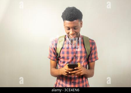 teenager nero che trasporta lo zaino utilizzando lo smartphone che esprimono ritorno a scuola, tecnologia, comunicazione, connessione online, e-learning, incontri, accademici Foto Stock
