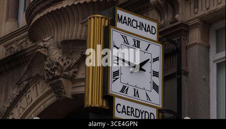 CARDIFF, Regno Unito - 8 AGOSTO 2025 - orologio tradizionale che mostra l'ora nel centro di Cardiff con una statua dell'aquila e la parola gallese Marchnad che significa mercato Foto Stock