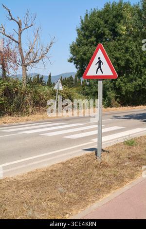 Primo piano di un segnale di avvertenza di attraversamento pedonale con sfondo campo. Un'immagine sulla sicurezza stradale, le regole e la cautela per i pedoni. Foto Stock