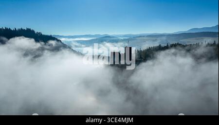 Polonia. Castello medievale di Niedzica che emerge dalla nebbia mattutina in autunno. Foto aerea del drone contro il sole di risciacquo. Montagne di Pieniny nel bac Foto Stock