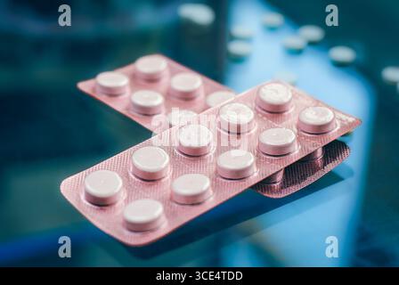 Le confezioni blister di varie pillole, incluse quelle arancioni e rosa, sono esposte contro una superficie riflettente. Alcune pillole gialle sfuse sono sparse in t Foto Stock