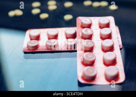 Le confezioni blister di varie pillole, incluse quelle arancioni e rosa, sono esposte contro una superficie riflettente. Alcune pillole gialle sfuse sono sparse in t Foto Stock