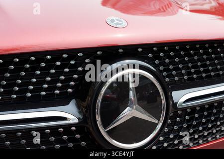 Primo piano del logo Mercedes-Benz argento centrato sulla griglia di un veicolo rosso con dettagli cromati e esagonali. Foto Stock