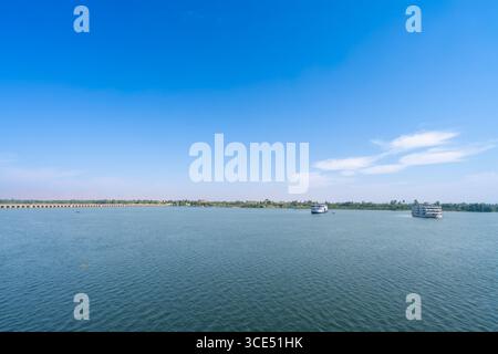 Ampia vista panoramica del Nilo con navi da crociera e ponte vicino a Esna Lock Egypt sotto uno splendido cielo blu con nuvole bianche. Foto Stock